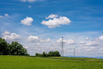 Obraz premium High voltage pylons and wires on the field. Landscape scene with agricultural field, trees, sky and clouds. Vevey, Switzerland.