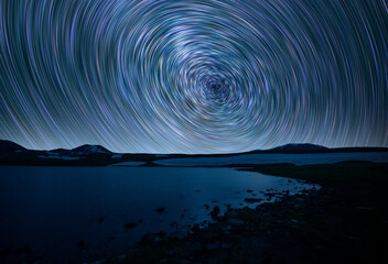 Beautiful small lake and mountains under the colorful star trails on the sky. Night time lapse photography.