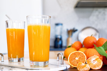 Ripe bio oranges and two glasses of fresh squeezed orange juice on the table of the kitchen. Organic Sicilian oranges.