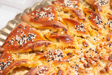 Piece of round cheese pie with green onion, dill, white sesame, black sesame