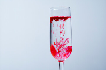 Red tattoo pigment dissolved in a glass of water. Hand stirring pigment in water