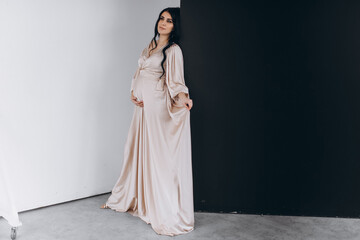 Fototapeta na wymiar Studio portrait of beautiful pregnant woman is wearing nice long dress and holding her belly