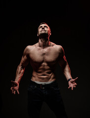 Fototapeta na wymiar Handsome sexy man with muscular body, showing a welcome gesture, standing on a black background. Sports, bodybuilding motivation. Dark studio shot with copy space portrait