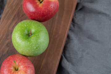 Red and green apples in a row on a wooden board