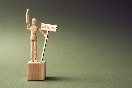 Coronavirus concept - wooden figure standing on a pedestal, raising hand and holding a sign with insctiption COVID-19