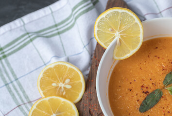 A white bowl of lentil soup with slices of lemon on a wooden board