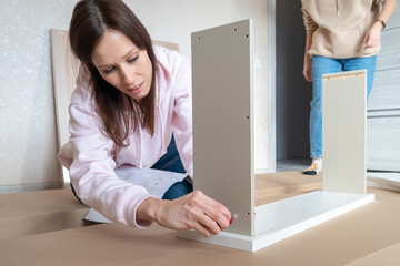 Young women putting together self assembly furniture as move into new house.