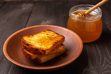 slices of bread dripped with honey in a ceramic plate with a jar of honey on a dark wooden background
