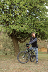 Fototapeta premium Sports brutal bearded guy on a modern mountain bike. Cyclist on the green hills in the spring.