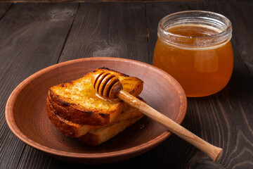 slices of bread dripped with honey in a ceramic plate with a jar of honey on a dark wooden background