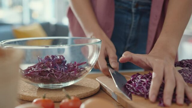 Hand of young Asian woman chef hold knife cutting Red Chinese cabbage on wooden board on kitchen table in house. Cooking vegetable salad, Lifestyle healthy food eating and traditional natural concept.