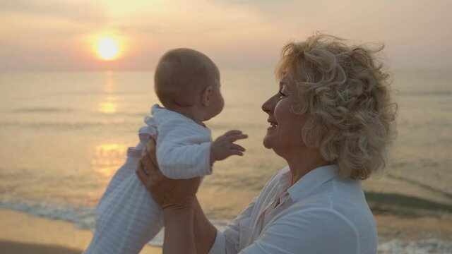 Happy grandmother holding her granddaughter in her arms by the sea