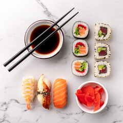Sushi rolls and nigiri sushi and soy sauce on a white stone background and chopsticks on the side....
