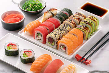 Traditional Asian food, sushi rolls, seaweed salad and ginger on a marble white table.