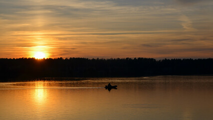 Naklejka premium Orange sunset over the lake with silhouette of fisherman boat. Selective focus.