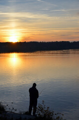 Fototapeta na wymiar Silhouette of fisherman on the background of orange sunset over the lake. Selective focus.