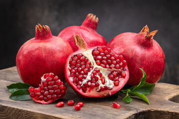 Healthy pomegranate fruit with leaves and open pomegranate on an old wooden board, side view, dark vintage background.
