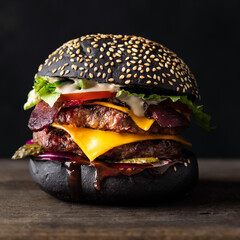 Fresh tasty burger with black bun and double beef patty on a black background.