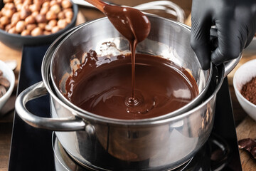 Confectioner prepares the melted dark chocolate in a bowl on a wooden table. Liquid hot chocolate. Confectionery. Cooking melted chocolate