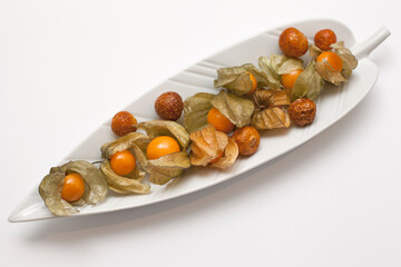 Golden Berry, Physalis or Cape Gooseberry - Healthy Tropical Yellow-Orange Fruit. Fresh and Dried Fruits on a white Plate shaped like a Banana Leaf.