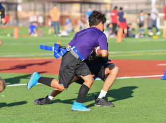 Young boy running the ball while playing in a flag football game