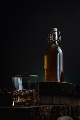 A glass of alcohol near a bottle. Old whiskey bottle on black wooden table. Drinks on a dark blurred background.