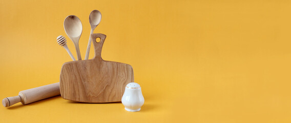 Banner :wooden kitchen utensils-board, spoons, rolling pin with salt shaker on a yellow background, side view, space for text
