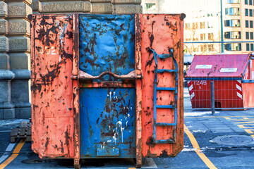 Large, heavily used, scratched and aged container for waste or construction sites in orange and blue in the city centre