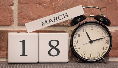 Important date, March 18, spring season. Calendar made of wood on a background of a brick wall. Retro alarm clock as a time management concept.