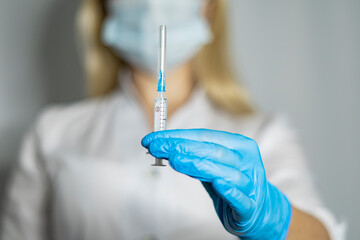 Female doctor with blue medical gloves holds a syringe