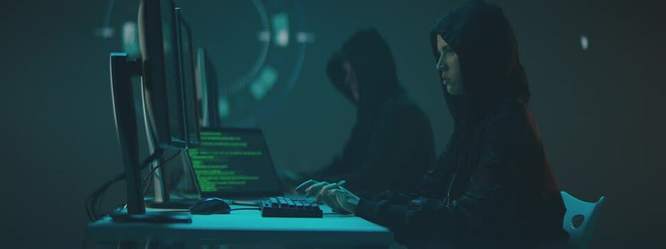 Hackers working in hi-tech workspace with a greenscreen computer displays and code animaton in background.