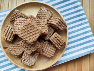 A pile of chocolate square waffles on a wooden plate with a striped tablecloth.