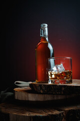 A glass of alcohol near a bottle. Old whiskey bottle on black wooden table. Drinks on a dark...