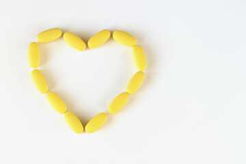 Yellow long pills laid out in shape of heart on white background, macro, close-up, copy space. Nutritional supplements concept, health, vitamins, trendy color of 2021, Illuminating. Horizontal
