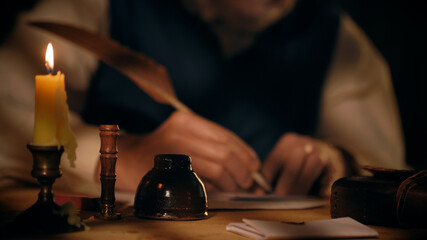 closeup vintage candle with man writing with a quill pen in background