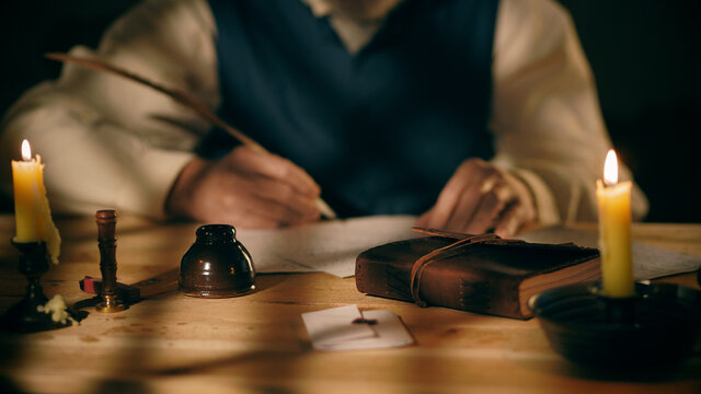 Out of focus man in background writing with a quill pen.