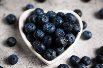 Fresh blueberries in a small heart shaped plate on a concrete background. Top view. Rustic. Healthy lifestyle
