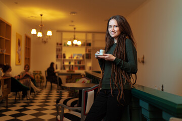 Drinking coffee. Pretty young woman holding cup of beverage at cafe.