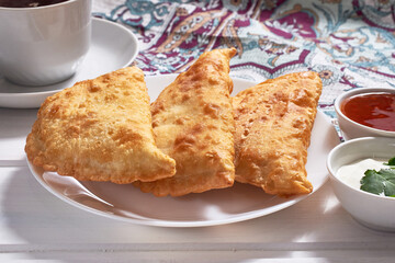 Delicious chebureks (calzone with meat) with sauces on a white wooden background.