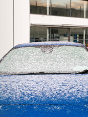 Brand new blue car covered with snow. Dealership in the background. Car sales in winter sales concept