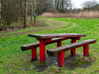 Old style red color wooden table and two benches in a park. Worn out surface.