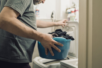 Adult man washing clothes using a top loading washing machine. Closeup on the hand holding a basin...