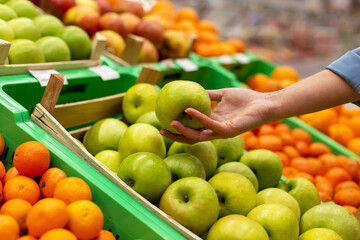 Picture of woman's hand holding a green apple in the supermarket. 
