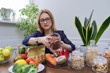 Middle aged woman professional nutritionist sitting at table with foods, hazel nuts