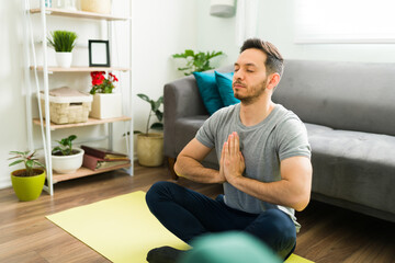 Adult man sitting in a yoga mat and meditating at home