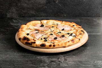 Hot tasty traditional italian pizza with salami, meat, cheese, tomatoes greens on a dark background