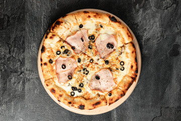 Hot tasty traditional italian pizza with salami, meat, cheese, tomatoes greens on a dark background
