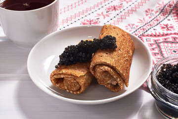 Pancakes with black caviar on a white wooden background. A traditional treat for Shrove Tuesday.