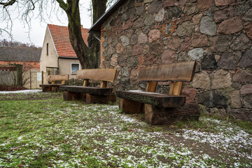 Oak benches near a stone wall. Wet snow on the ground.