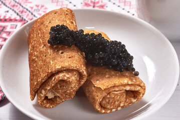 Pancakes with black caviar on a white wooden background. A traditional treat for Shrove Tuesday.